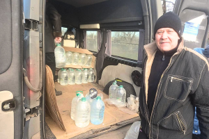 Ukrainian man standing next to back of the van with water bottles